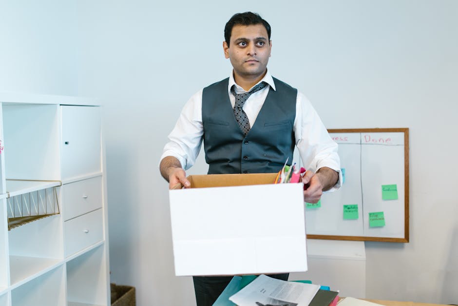 A close-up view of a stack of white paper photocopiers or printers with the brand name 'KITCHEN' printed on a paper label attached to the top device, situated on a brown cardboard box labeled 'BOOKS'