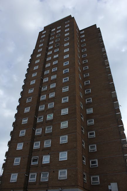 A tall, multi-storey residential building constructed from brown brick, with numerous small, rectangular windows aligned in vertical columns across its façade. The building extends upward into a clou